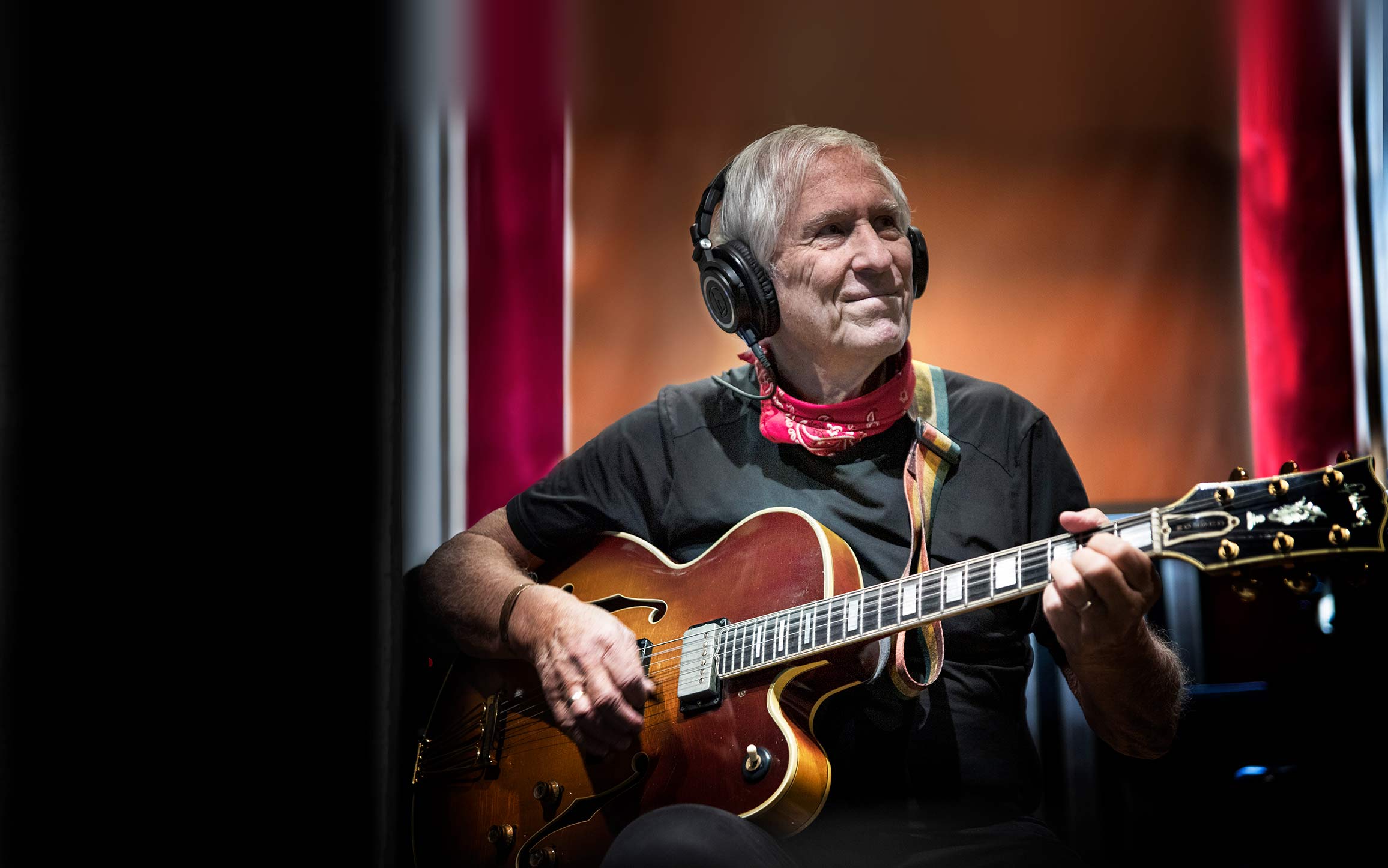 Nick Binkley sitting playing his guitar with headphones on